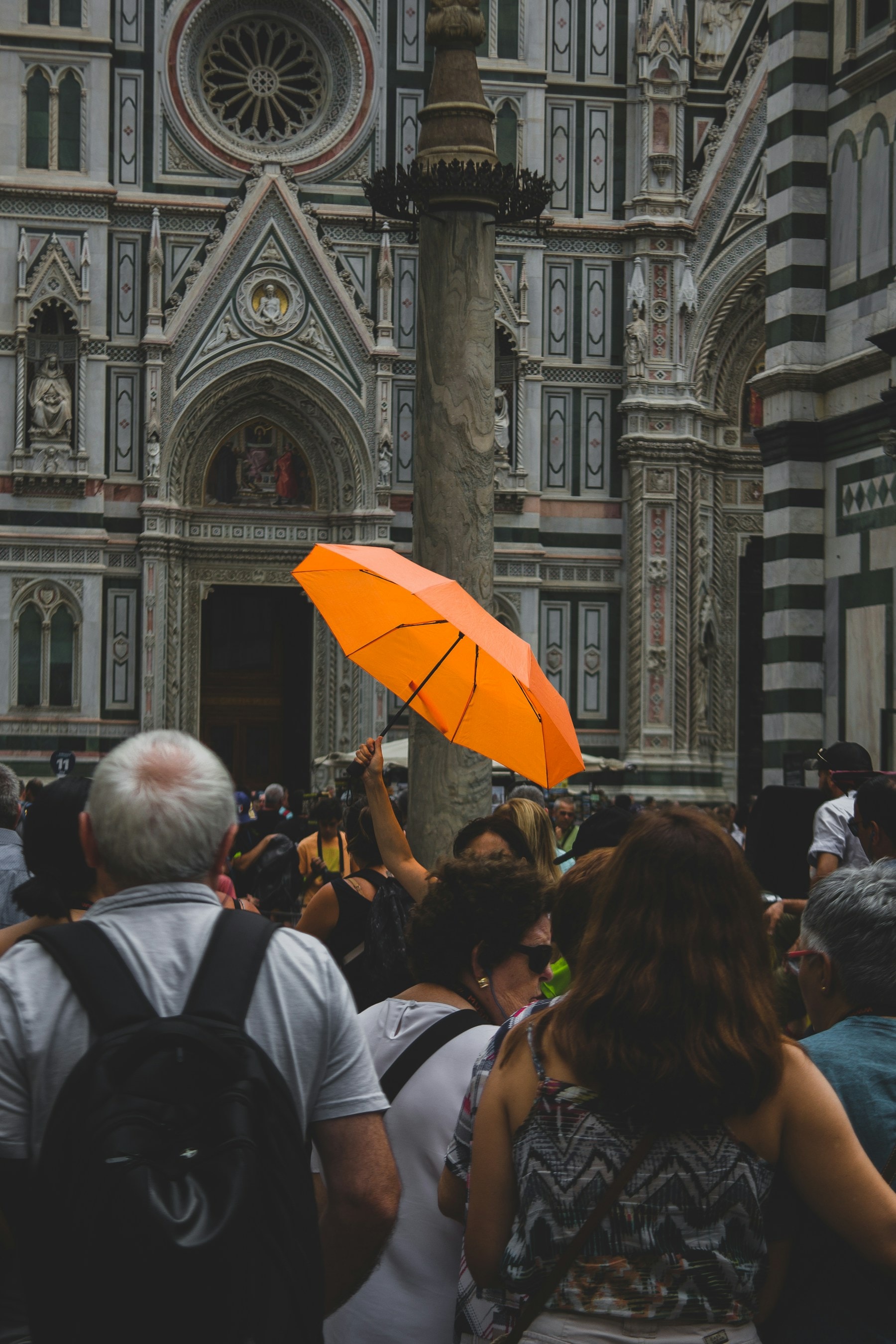 A tour guide holds up an orange umbrella for her group outside Florence Cathedral