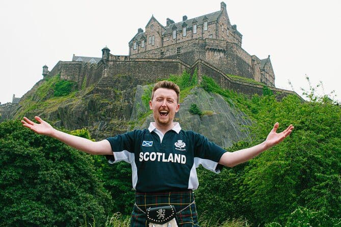 A guide in a Scotland shirt with arms out below Edinburgh Castle